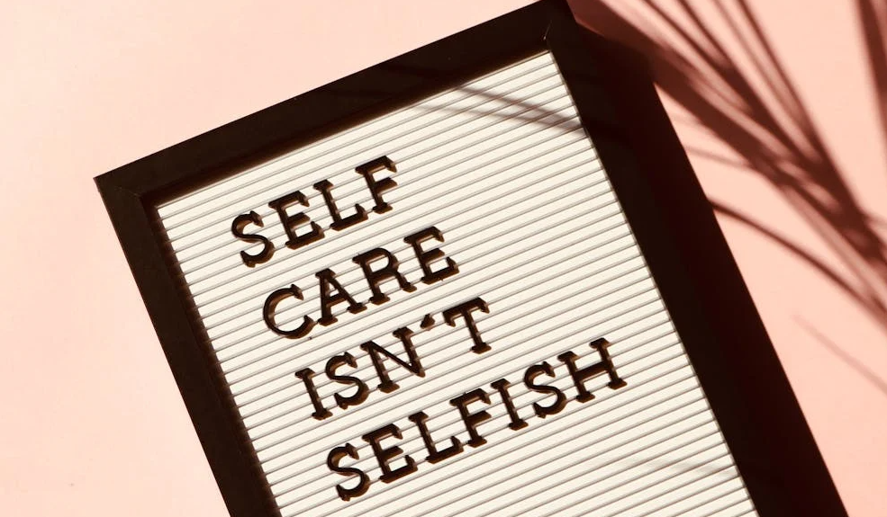 White letter board with black letters spelling ‘SELF CARE ISN’T SELFISH,’ set against a pale pink background.